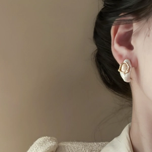 Detail of baroque pearl earring with golden hexagonal metal frame on female model's ear