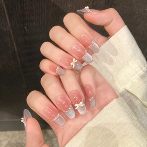 Close-up of nude pink cat eye press-on nails with white 3D bows and rhinestones