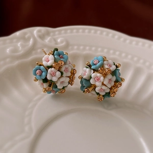 Close-up of elegant floral cluster stud earrings with blue ceramic roses and gold crystals