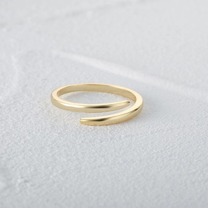 Macro shot of minimalist gold open spiral ring with polished finish on textured background