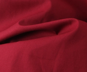 Gros plan du tissu rouge foncé montrant le tissage fin et le drapé doux pour la robe