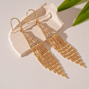 Détail de boucles d'oreilles dorées avec triangle en zircon et pampilles élégantes