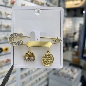Detail of a gold safety pin brooch featuring a Hamsa hand, crown, and coin charms