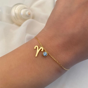 Detailed shot of a gold Aries zodiac bracelet featuring a blue gemstone on a woman's wrist