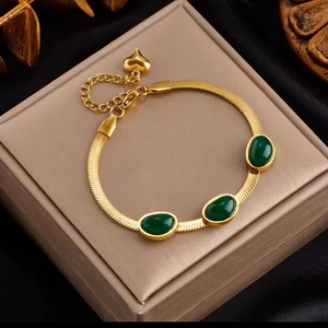 Details des goldenen Schlangenketten-Armbands mit drei smaragdgrünen Steinen und Herz