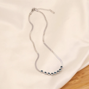 Silver snake chain necklace with blue evil eye charms on beige silk fabric background