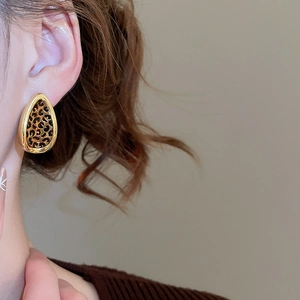 Close-up of leopard print leaf earrings with gold metal edges worn on model's ear