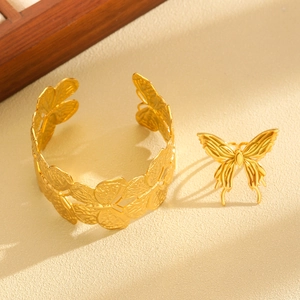 Detailed view of luxury gold butterfly bangle and matching ring on a textured background