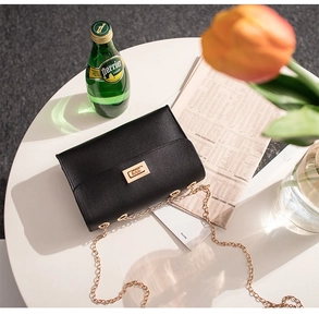 Close-up of black lychee-textured crossbody bag with golden chain and lock on a table