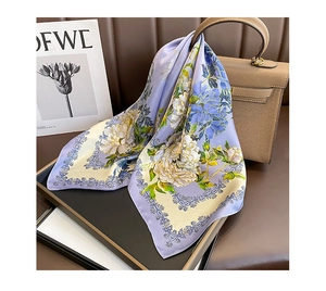 Folded purple silk scarf with yellow floral print on a tray next to a leather handbag