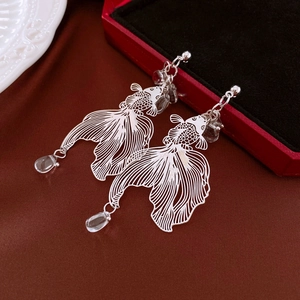 Dettaglio orecchini a pesce rosso in argento con perle a goccia su seta rossa lussuosa