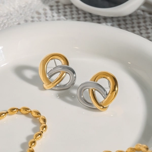 Zweifarbige Herz-Knoten-Ohrringe in Gold und Silber auf einem weißen Porzellanteller
