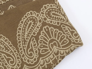 Gros plan sur la broderie paisley beige sur le tissu marron du gilet ethnique