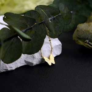 Elegante 18K vergoldete Schmetterling-Halskette auf weißem Stein mit Eukalyptusblättern
