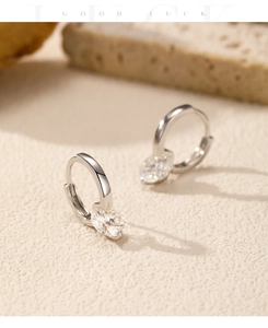 Macro detail of silver hoop earrings with oval moissanite stones on textured paper