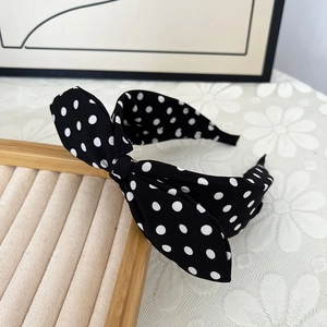 Detailansicht eines schwarz-weißen Polka-Dot-Haarreifens mit klassischer Schleife auf Holz