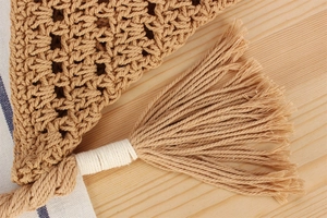 Macro detail of hand-woven hollow triangular bag with natural fringe and wood texture background