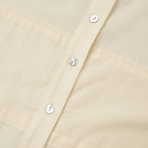 Macro detail of beige linen shirt with textured fabric and pearlescent buttons