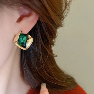 Close-up of vintage geometric gold earring featuring a large emerald green square gemstone