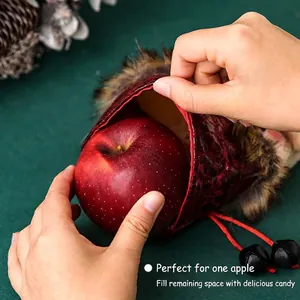 Red plush Christmas gift bag with bell drawstrings being filled with an apple