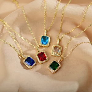 Macro shot of colorful square zircon pendants with emerald and sapphire stones on beige silk