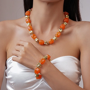 Close-up of geometric orange acrylic beads and gold twisted charms on necklace and bracelet