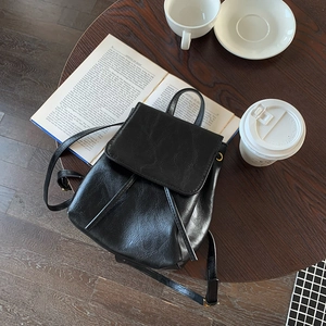 Dettaglio di uno zaino minimalista in pelle nera con coulisse su un tavolo di legno rustico