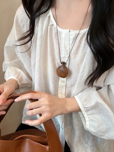Close-up of wood gourd pendant necklace on white linen shirt for a natural aesthetic