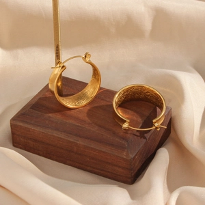 Fashionable gold hoop earrings with brushed metal texture on a wooden stand