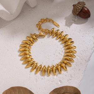 Detail of a chunky gold bullet-shaped link bracelet on a textured white surface