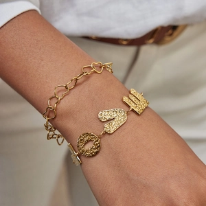 Gold layered heart and hammered letter bracelets on woman wrist with white shirt