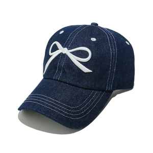 Close-up of white bow embroidery and contrast stitching on dark blue denim baseball cap