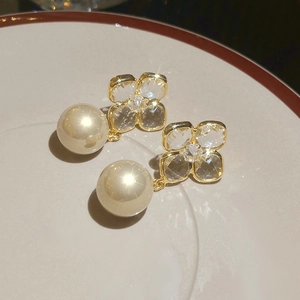 Macro view of gold-plated clover crystal earrings with dangling white pearl details