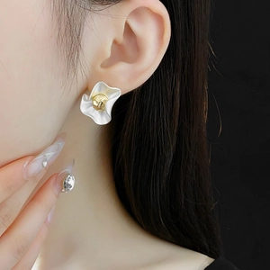 Close-up of elegant gold textured sphere earrings with white wavy petal design on model