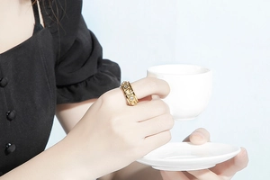 Détail d'une bague coeur dorée avec des pierres de zircon portée avec une tasse blanche