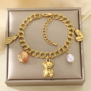 Detailed view of a gold titanium bracelet with pineapple, bear, and pearl charms on silk