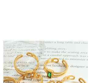 Detail of gold woven rings with rectangular green and white gemstones on a book page