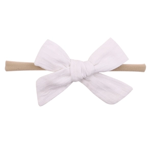 Detail of white cotton linen bow on a beige soft nylon elastic headband for infants
