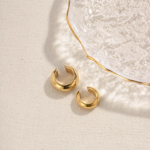 Golden C-shaped stainless steel ear cuffs set shown on a textured beige fabric background