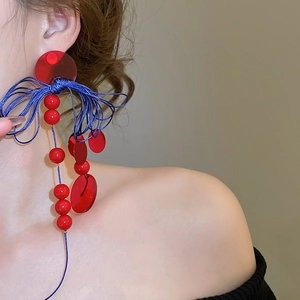 Detail of red acrylic discs and blue woven ropes on a geometric drop earring