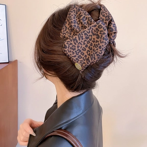 Detail of leopard print bow hair claw with gold metal tag worn on dark hair