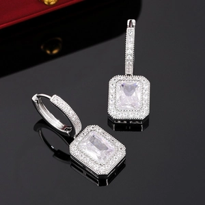 Sparkling silver halo hoop earrings with emerald-cut stones on a reflective black background