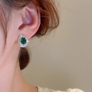 Close-up of emerald green zircon earrings with silver needle on a model's ear