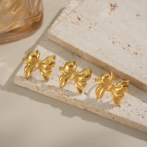 Polished golden bow stud earrings with 3D ribbon design on a textured stone base