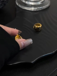 Close-up of gold leopard print cutout earrings worn by hand on a textured background