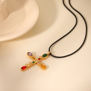 Detailed macro view of gold cross pendant with colorful gemstones on black rope chain