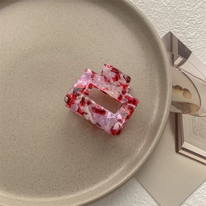 Dettaglio di una pinza per capelli rettangolare in acetato marmorizzato rosso su vassoio
