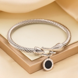 Macro detail of silver cable twist bracelet with black Roman numeral charm on silk cloth