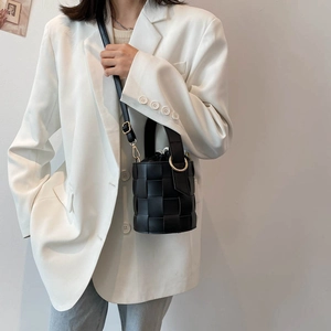 Chic black woven leather bucket bag with gold rings shown on model in minimalist setting
