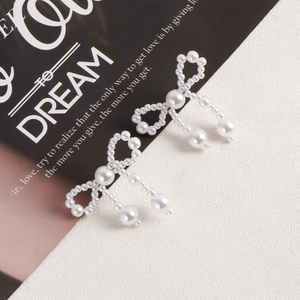 Elegant white faux pearl bow earrings with spherical pendants on a stylized background